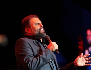 Bispo JB Carvalho de pé no palco do Modeladas Mais 2026 conduzindo a oração