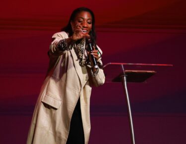 Demetria Stallings ministrando no palco do Modeladas Mais 2026, apontando para o público, ao lado da intérprete