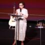 Dra. Ilma Cunha pregando no palco do Modeladas Mais 2026, com o violão e o telão ao fundo