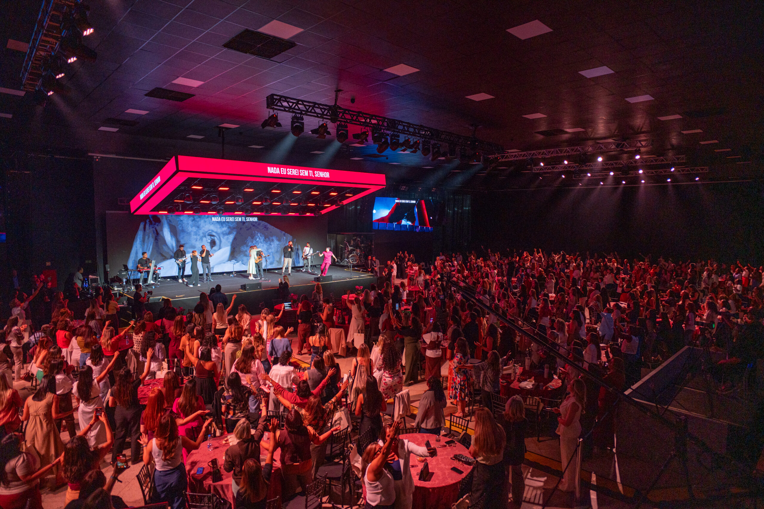 Plateia do Modeladas Mais 2026 com o palco iluminado ao fundo, na Comunidade das Nações