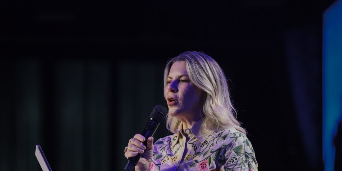 Bispa Dirce Carvalho, de camisa florida, fala ao microfone durante a pregação na Conferência Global 2026
