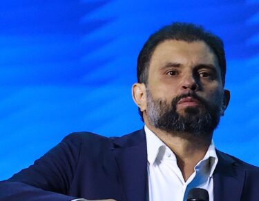 Bispo JB Carvalho, de barba e terno azul-marinho, diante do painel azul