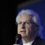 Charles Scott, de cabelos brancos e óculos, fala ao microfone na Conferência Global 2026