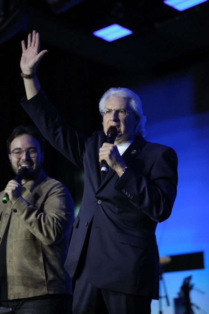 Charles Scott levanta a mão enquanto prega, ao lado do intérprete