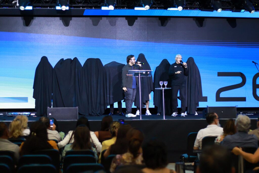 Charles Scott no palco ao lado de figuras cobertas por mantos pretos que representam os filhos de Saul