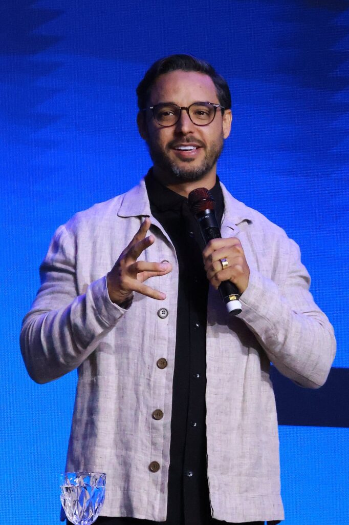 Pr. Junior Cabral sorri e gesticula enquanto fala ao microfone