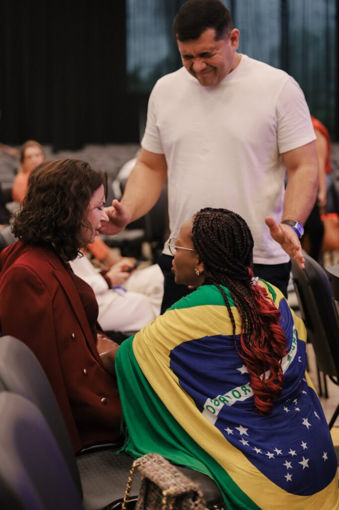 Um homem ora com a mão estendida sobre duas mulheres, uma delas envolta na bandeira do Brasil