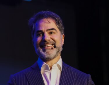 Victor Sorrentino sorri no palco, de terno risca de giz e microfone de lapela, na Conferência Global 2026